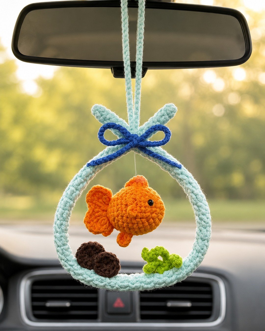 Close view of the goldfish ornament on a car mirror in warm evening light, showing the crocheted fish and bow