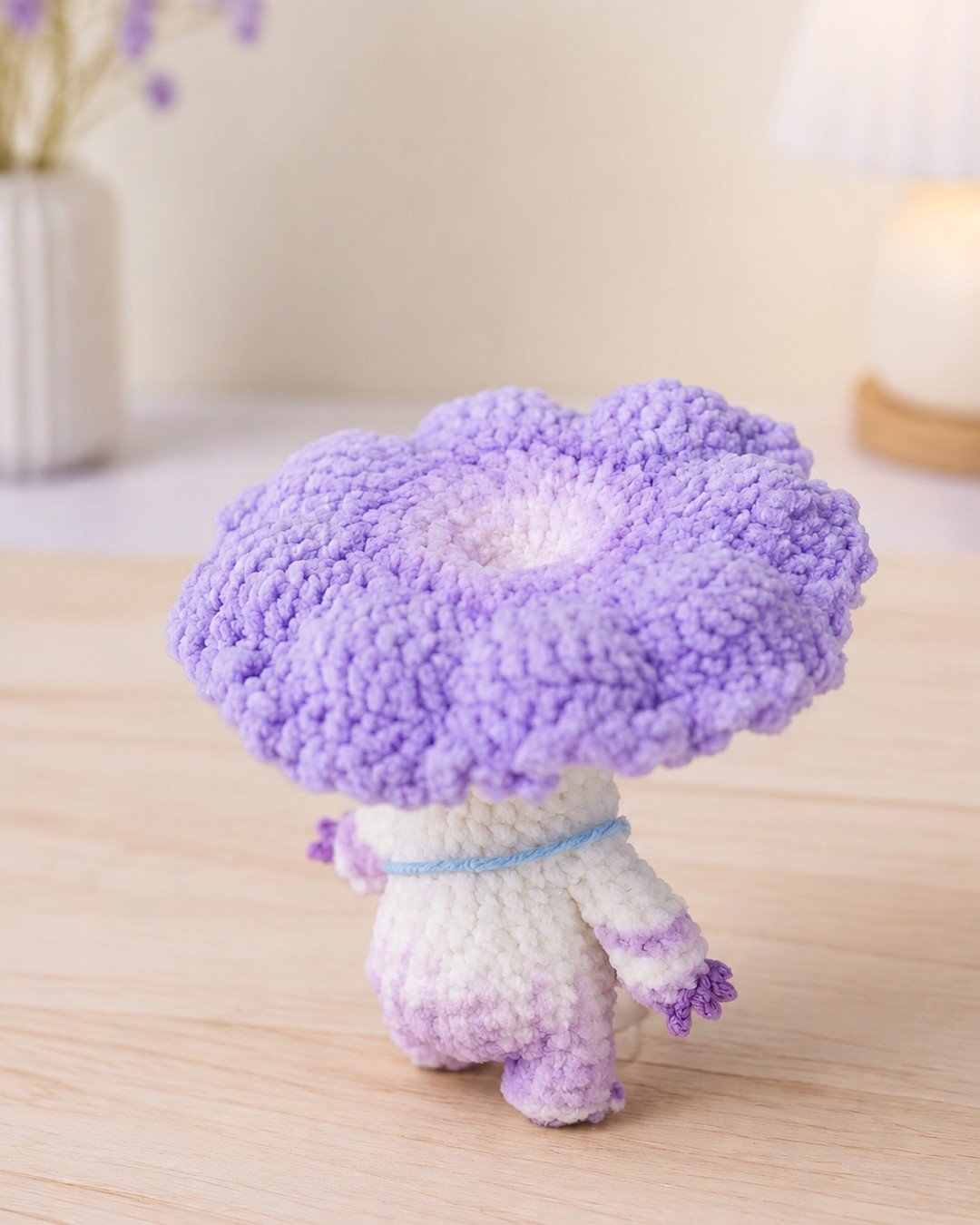 Back view of the mushroom doll showing the ruffled underside of the cap and the blue bag strap across its back